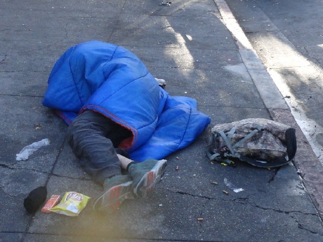 Homeless person lays on sidewalk Berkeley California with food from the little way homeless outreach charity